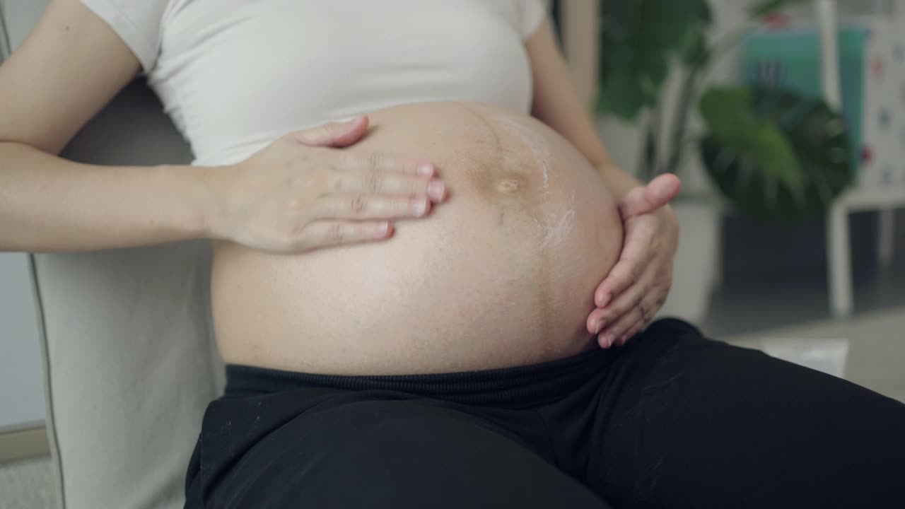 孕妇在家里把润肤霜涂在腹部视频素材