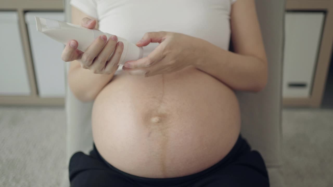 孕妇在家里把润肤霜涂在腹部视频素材