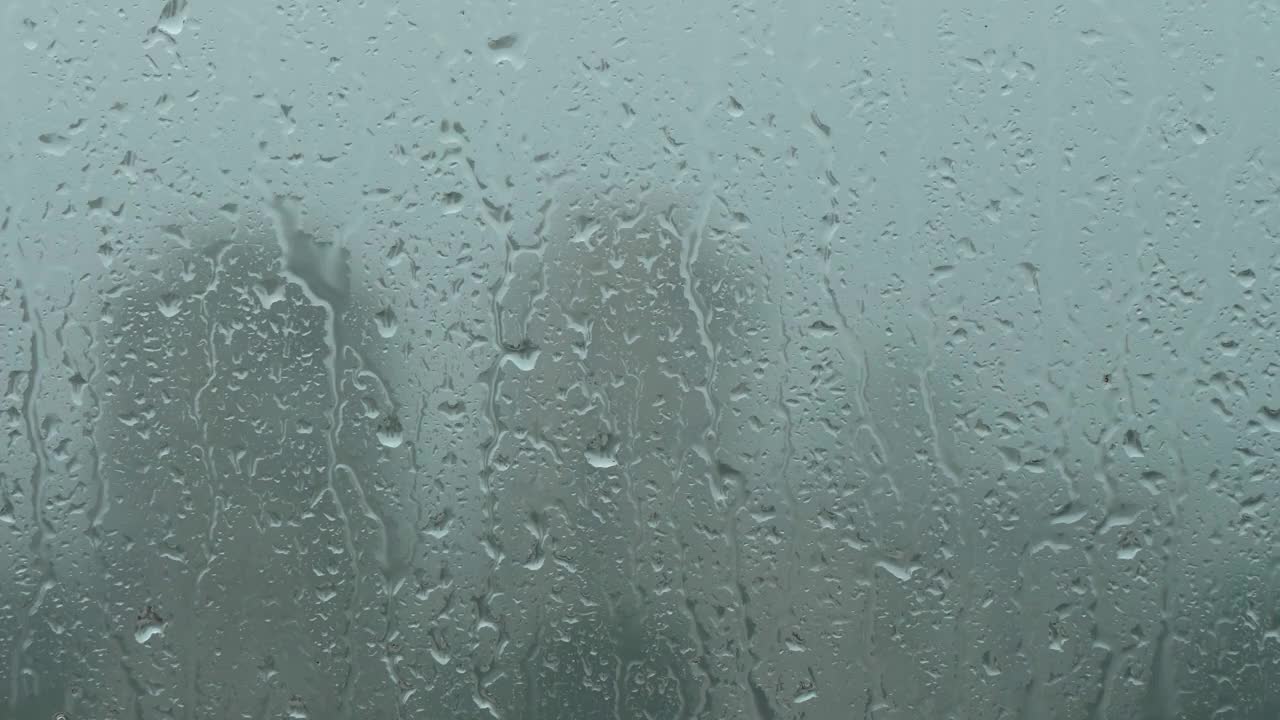 大雨期间，水滴滴在潮湿的窗户玻璃上，与城市中高层住宅的轮廓模糊的背景相映衬视频素材