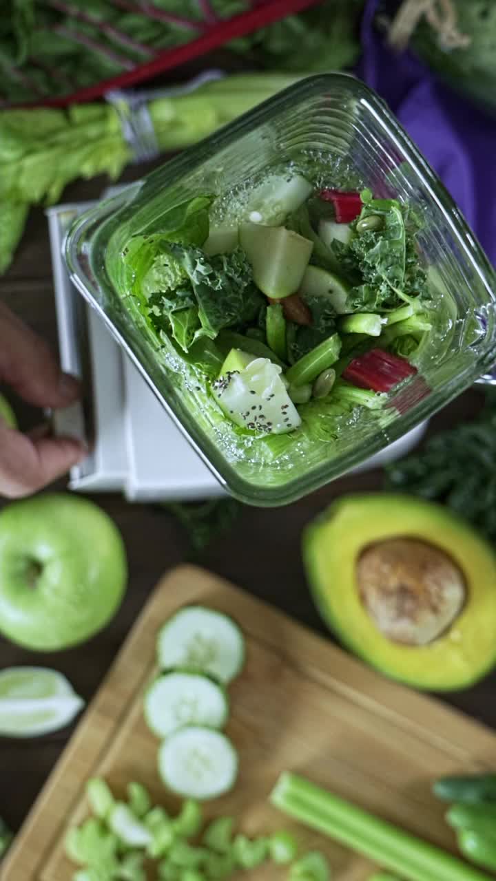 饮食理念:下面的慢镜头是搅拌机在搅拌蔬菜和水果来制作排毒奶昔。切菜板和搅拌机在餐桌上搅拌视频素材