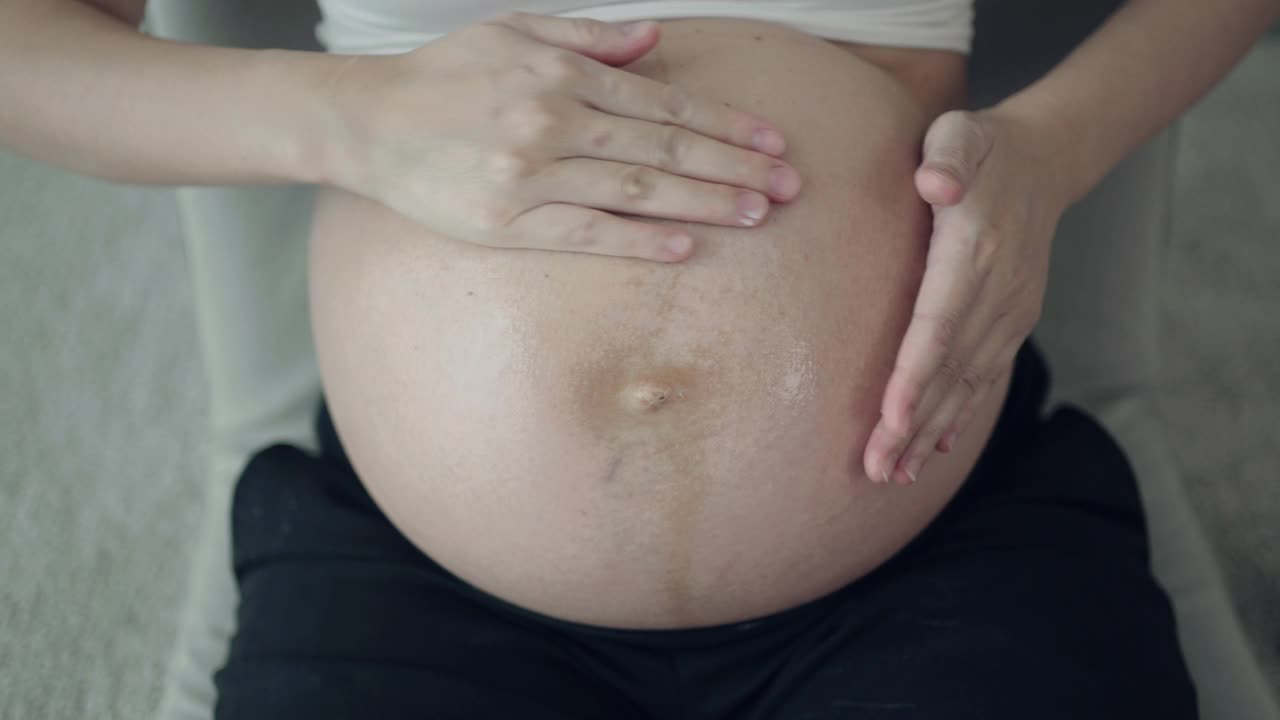 孕妇在家里把润肤霜涂在腹部视频素材