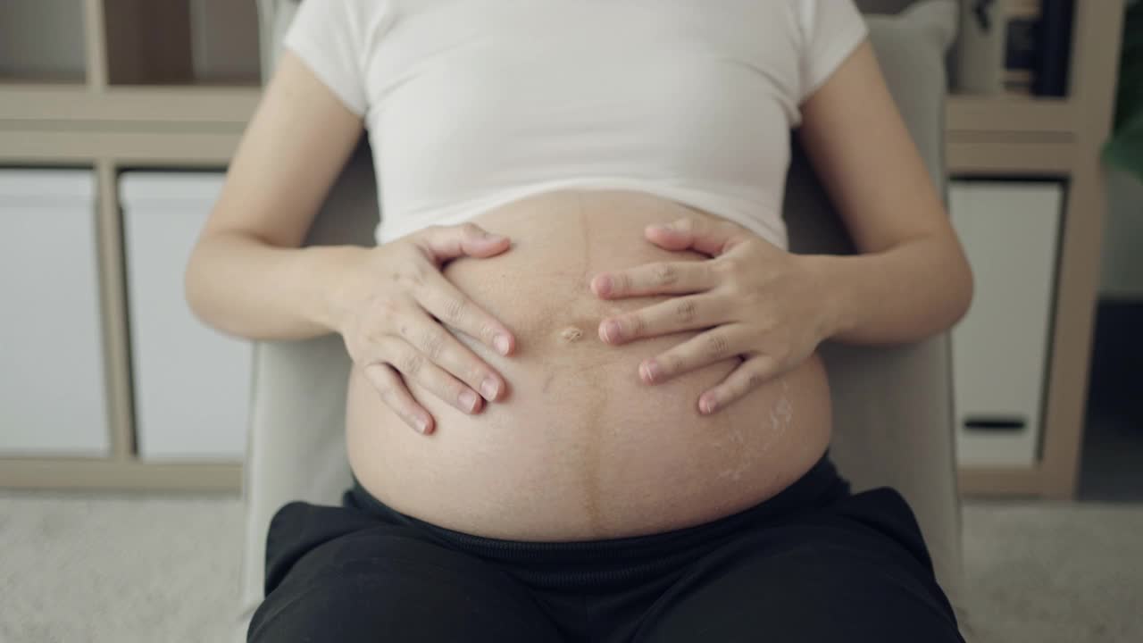 孕妇在家里把润肤霜涂在腹部视频素材