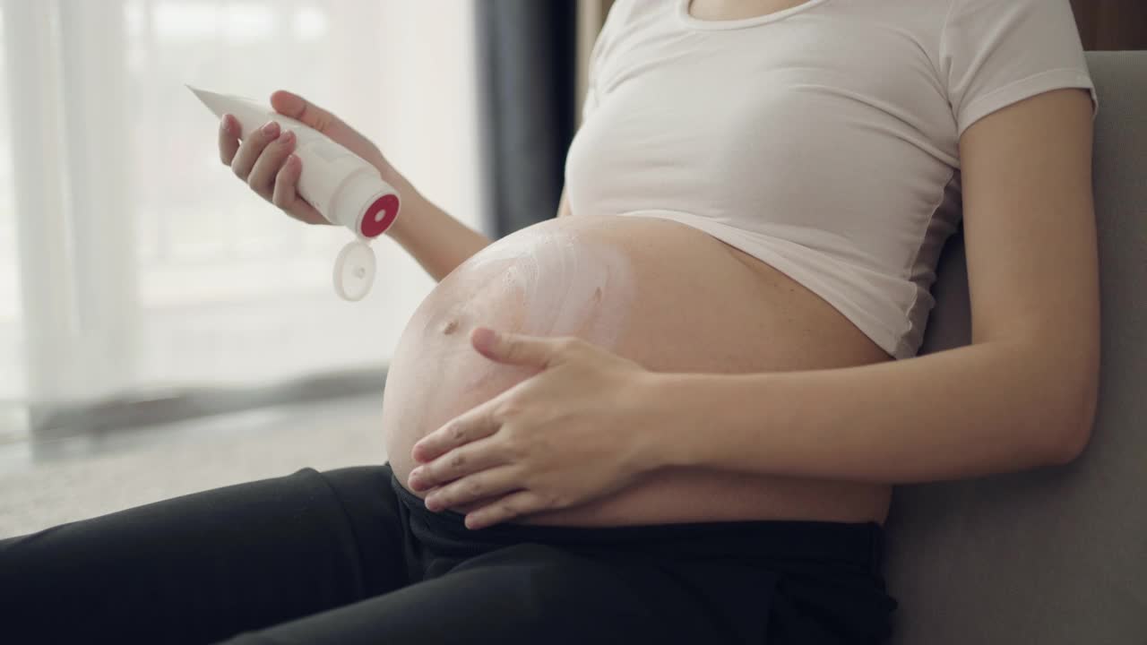 孕妇在家里把润肤霜涂在腹部视频素材