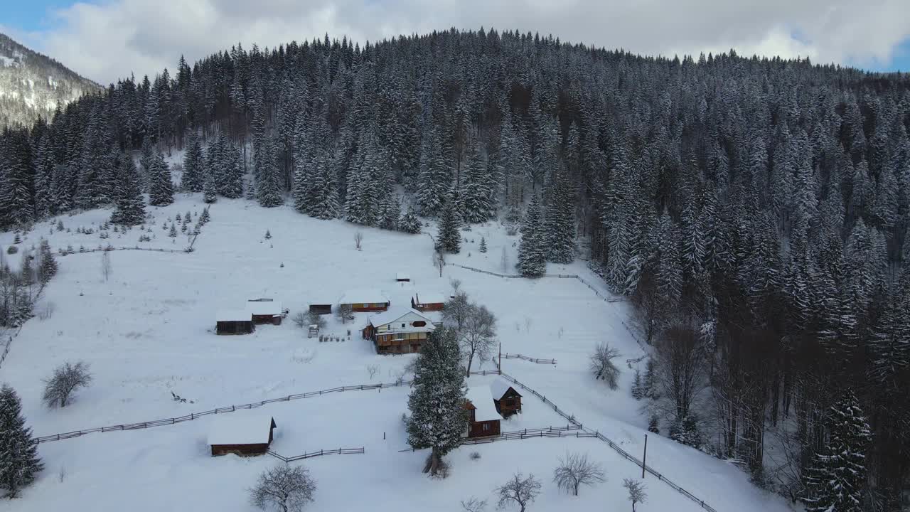 空中冬季景观与小乡村房屋之间的雪覆盖森林在寒冷的山。视频素材