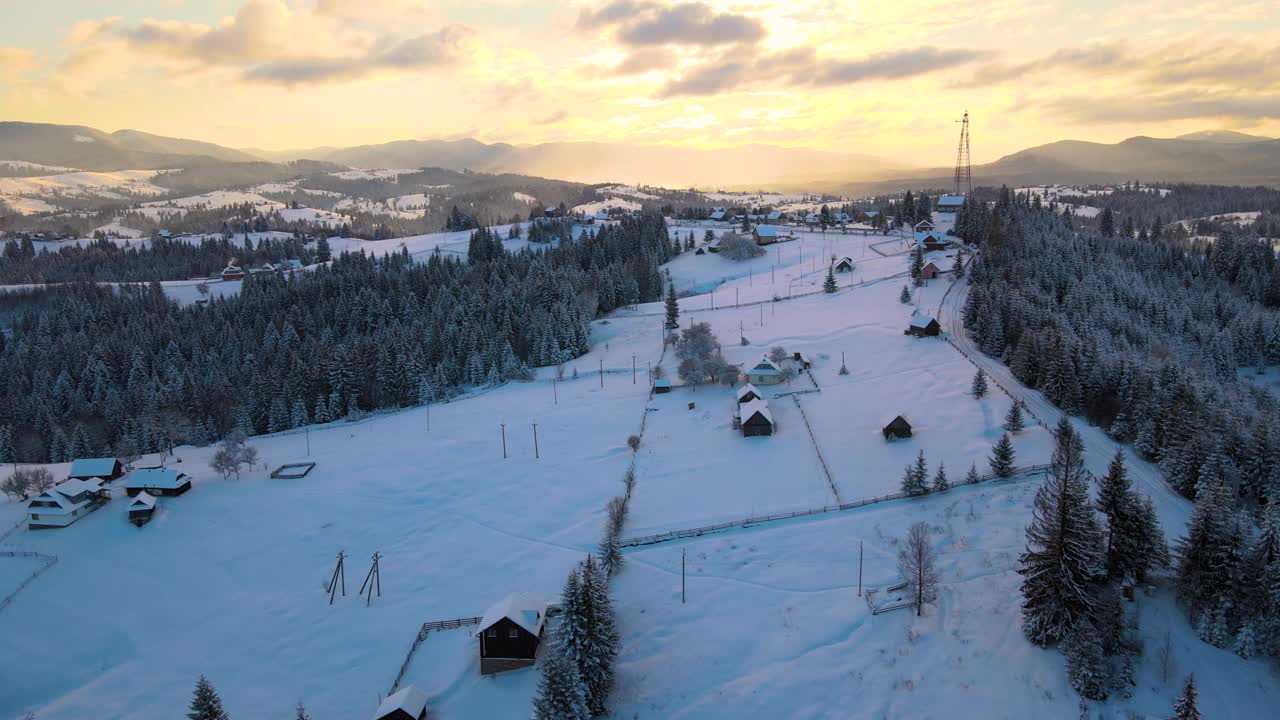 空中冬季景观与小村庄房屋之间的雪覆盖森林在寒冷的山在晚上。视频素材