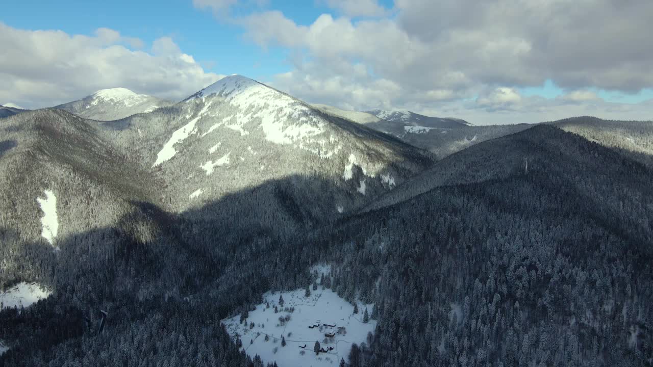 空中冬季景观与小乡村房屋之间的雪覆盖森林在寒冷的山。视频素材