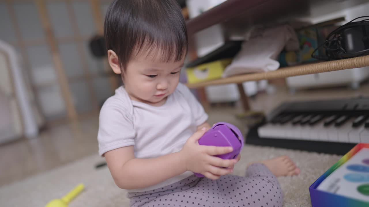 活泼可爱的亚洲幼童喜欢一起愉快地敲打紫色玩具，牙齿微笑的女婴喜欢为她的玩具制作音乐，玩学，模仿和学习能力的童年视频素材