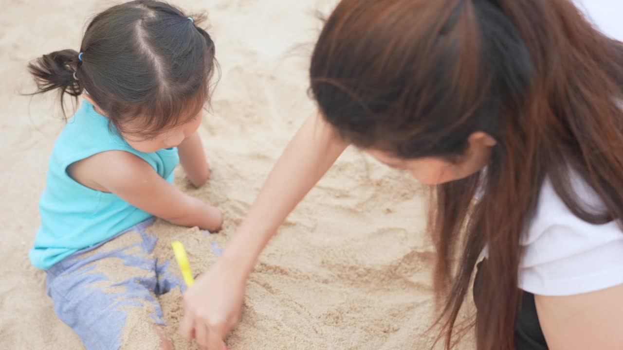 快乐的小女孩和妈妈玩沙子。使沙塔视频素材