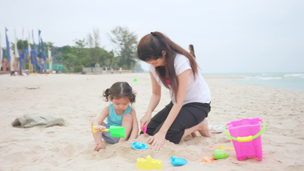 快乐的小女孩和妈妈玩沙子。使沙塔视频素材