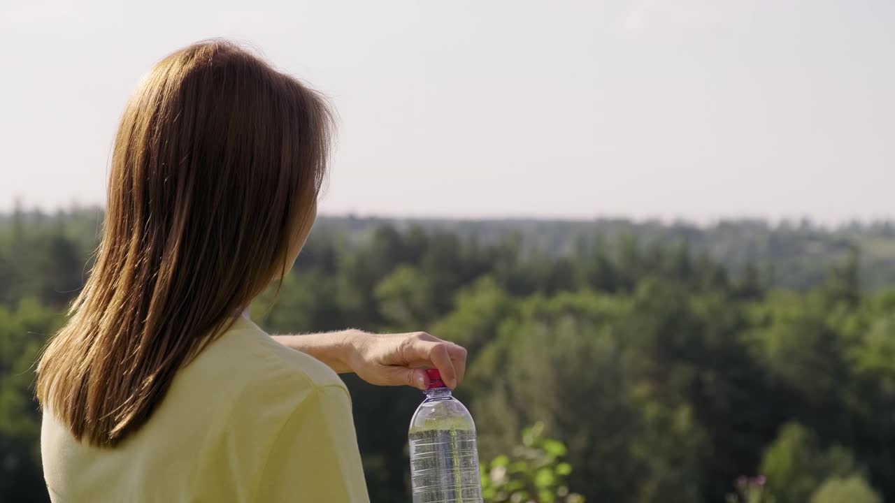 一个女人在炎热的夏日从瓶子里喝水。视频素材