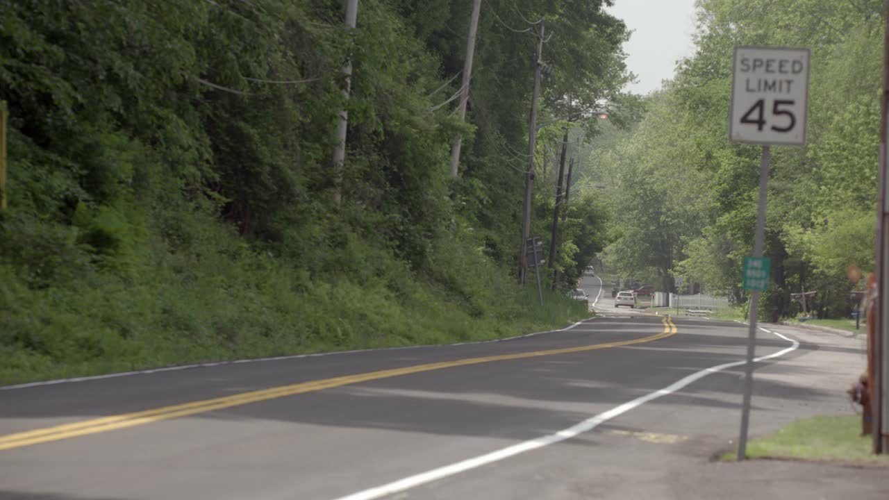 从右到左行驶在乡村道路上的汽车。树木和电线杆连接着道路。视频素材