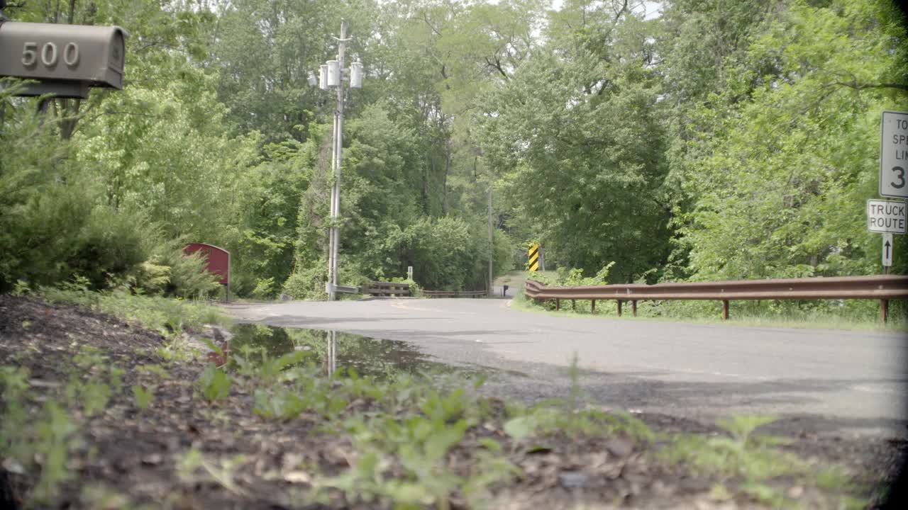 乡村道路弯角大。可见树木和限速标志。邮箱在fg中可见。在bg中可见的电话杆。可能是郊区。视频素材