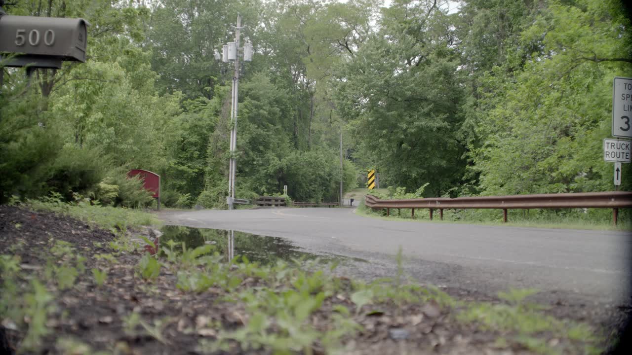 乡村道路弯角大。可见树木和限速标志。邮箱在fg中可见。在bg中可见的电话杆。可能是郊区。汽车和卡车在路上行驶。视频素材