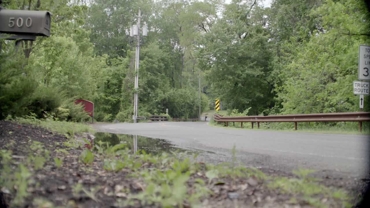 乡村道路弯角大。可见树木和限速标志。邮箱在fg中可见。在bg中可见的电话杆。可能是郊区。汽车和卡车在路上行驶。视频素材