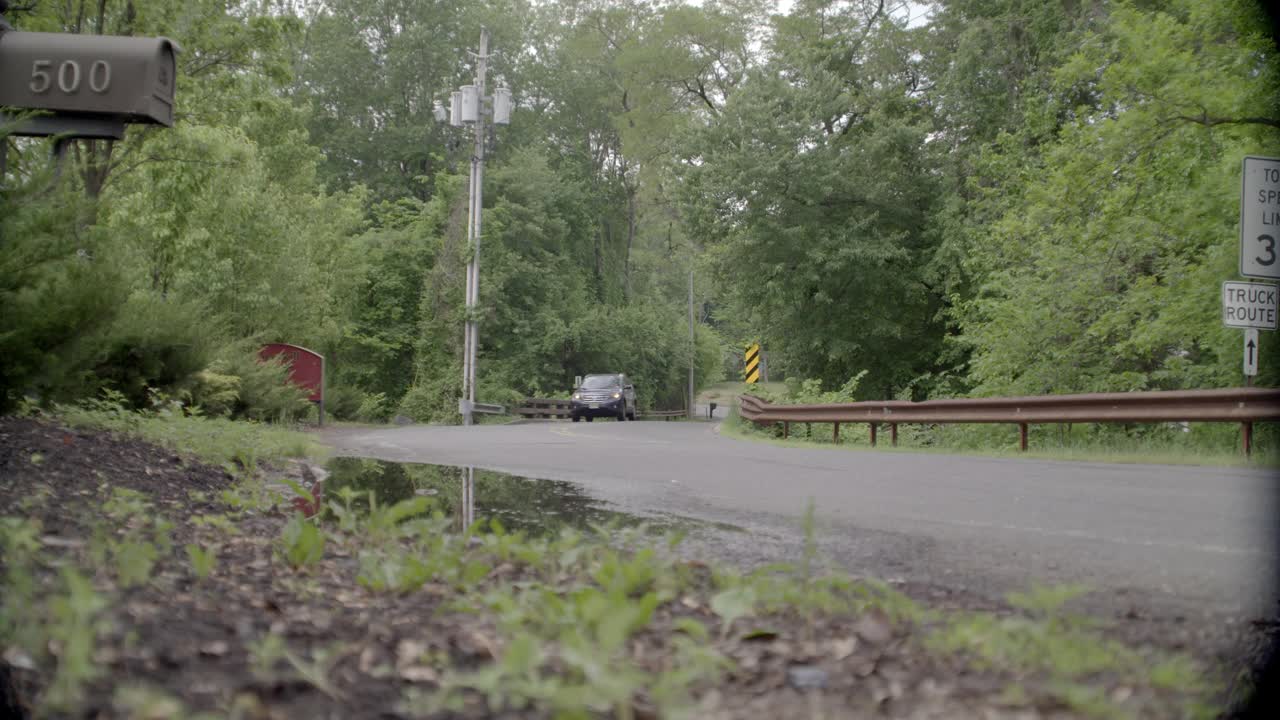 乡村道路弯角大。可见树木和限速标志。邮箱在fg中可见。在bg中可见的电话杆。可能是郊区。汽车和越野车在路上行驶。视频素材