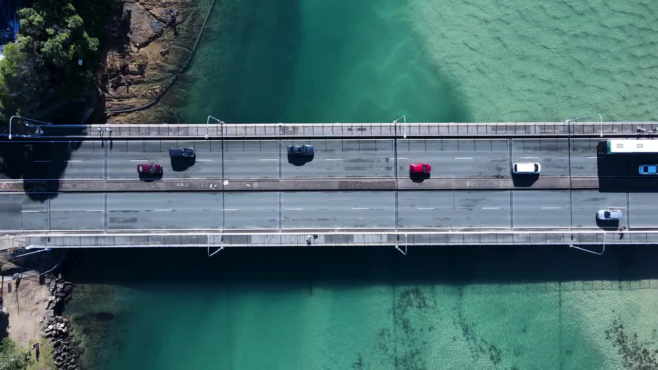 机动车和行人在横跨风景优美的海洋河口的桥上行驶。平移无人机视图视频素材