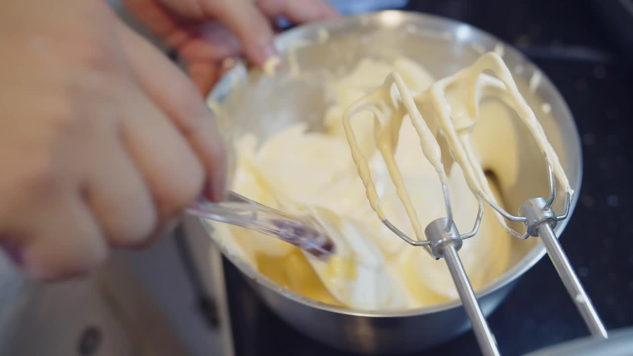 慢动作接近糕点师的手搅拌原料烤奶油蛋糕与面粉、鸡蛋、黄油和糖在一个碗里，在厨房准备甜点，接近自动面粉搅拌机视频素材