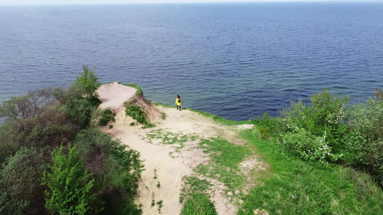 无人机拍摄的悬崖和女人在上面行走，看着大海视频素材