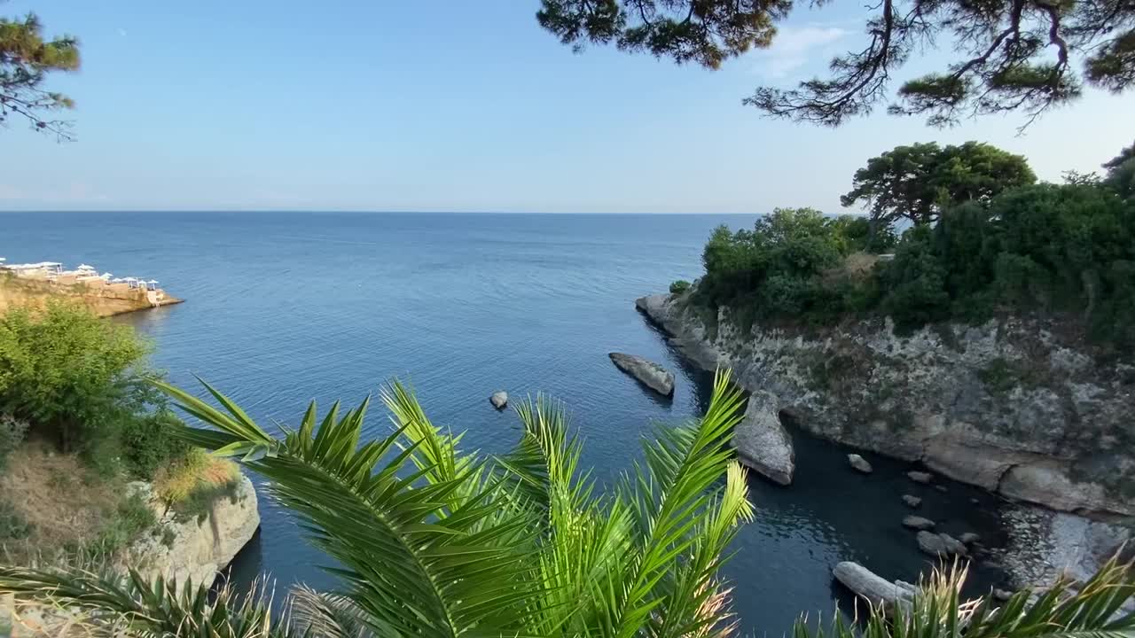 地中海沿岸岩石嶙峋，风景秀丽。海边有棕榈树和松树。平静的蓝色的大海。风景优美的小岛。夏天。放松。宁静。视频素材