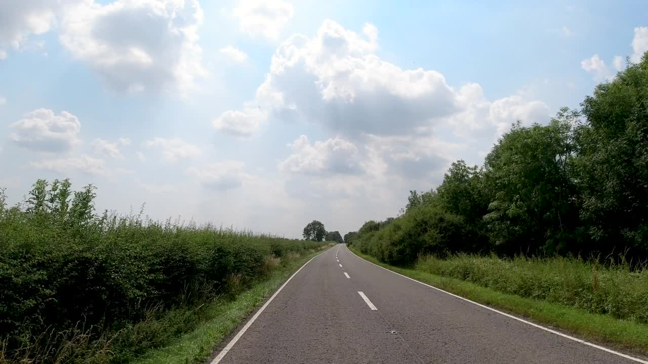4K实时POV汽车驾驶在漫长的蜿蜒的乡村道路在英国，英国。农场，田野和树篱路在一个阳光灿烂的蓝天。非城市场景的观点视频素材