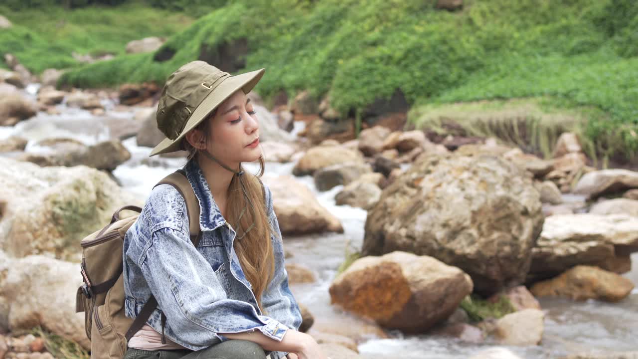 4K亚洲女人坐在小溪边的岩石上视频素材