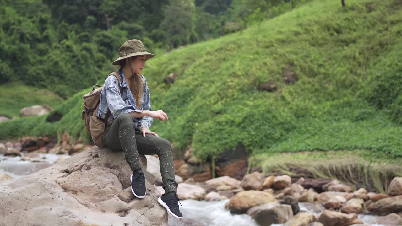 4K亚洲女人坐在小溪边的岩石上视频素材