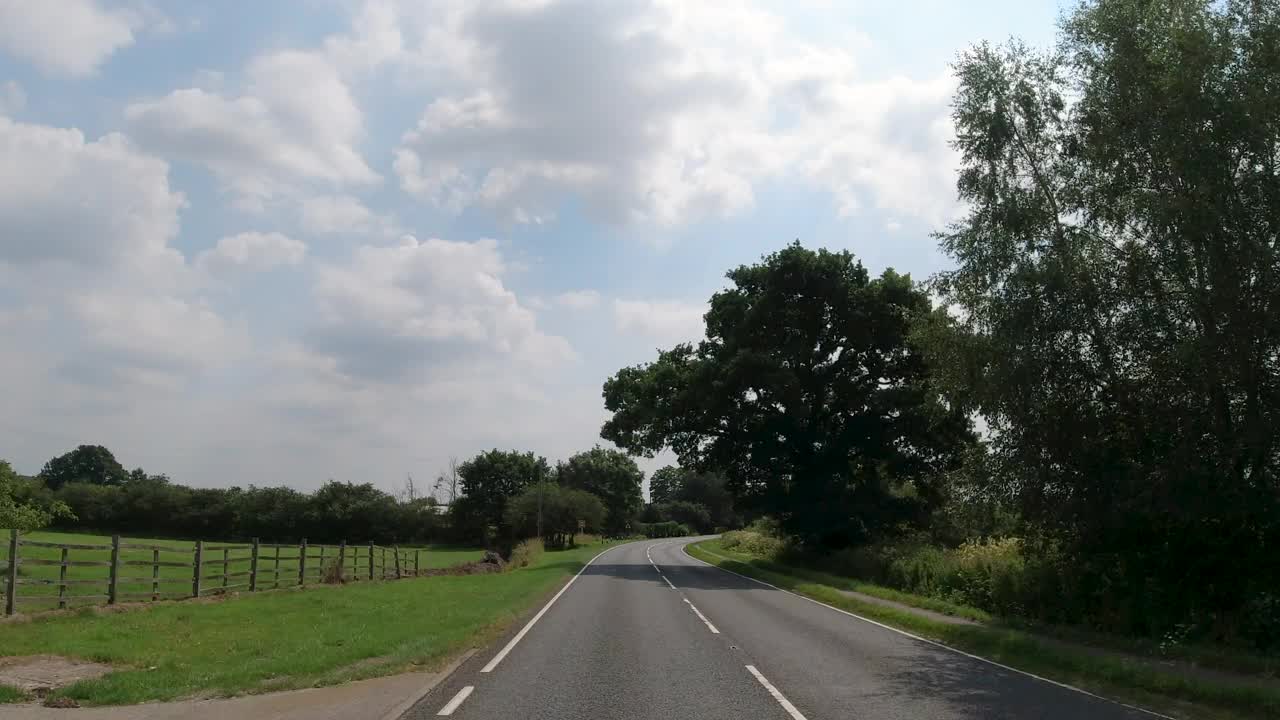 4K实时POV汽车行驶在漫长的曲折的乡村道路上，英国英格兰。农场，田野和树篱路在一个阳光灿烂的蓝天。非城市场景的观点视频素材