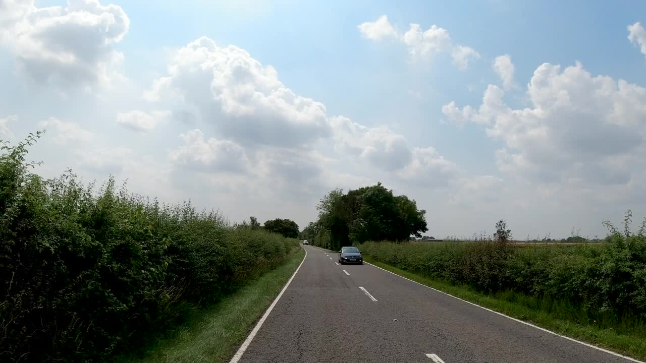 4K延时POV汽车行驶在漫长的乡村公路在英国，英国。农场，田野和树篱路在一个阳光灿烂的蓝天。非城市场景的观点视频素材