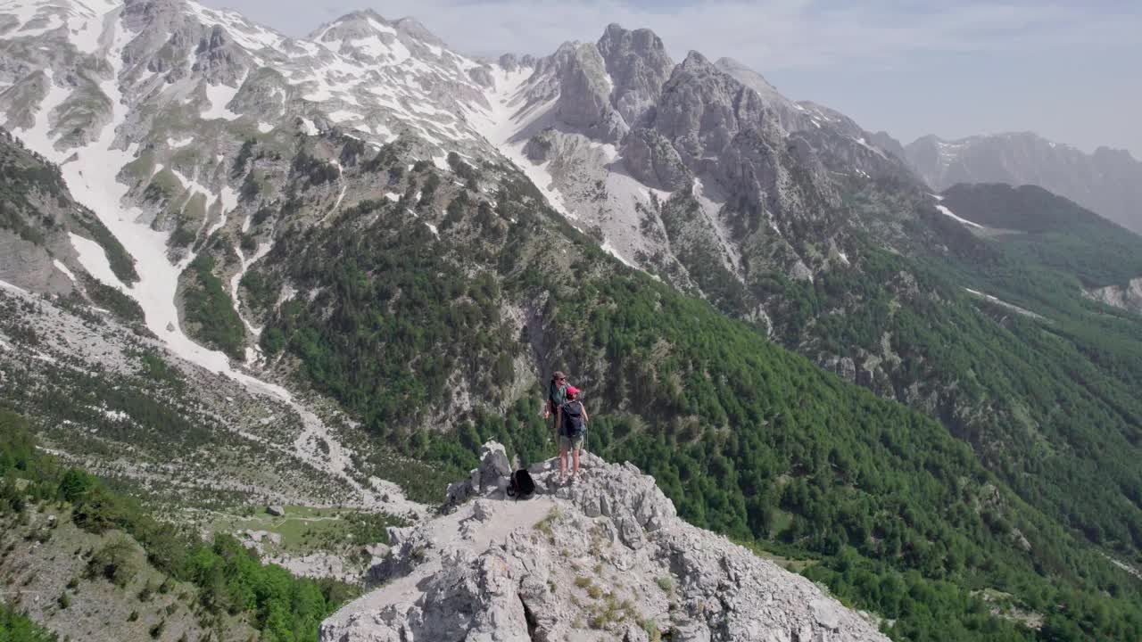 在山顶绕着两个背包旅行者飞行。一对夫妇爬到岩石山顶。挑战、风险和成功的概念视频素材