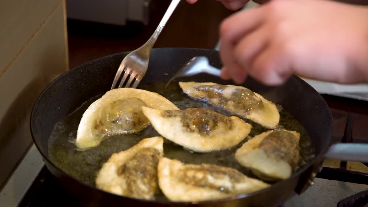 大厨用手在热煎锅里煎蘑菇饺子的特写镜头。在油里煮的金黄酥脆的饺子。视频素材