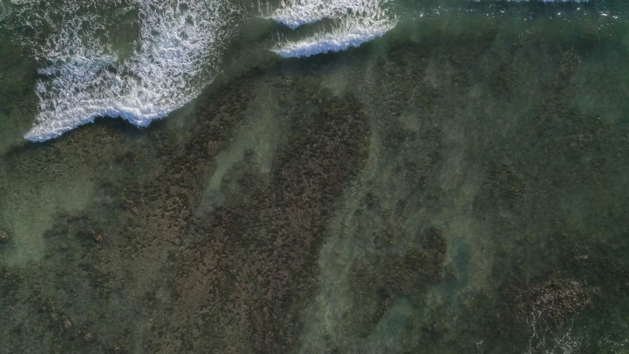 无人驾驶飞机在海面上飞行。垂直向下看的海洋表面。摄像机从右到左在海浪上移动。在水下可以看到岩石和暗礁。海洋有非常干净和透明的水视频素材