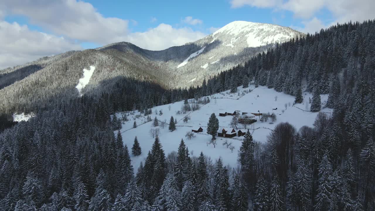 空中冬季景观与小乡村房屋之间的雪覆盖森林在寒冷的山。视频素材