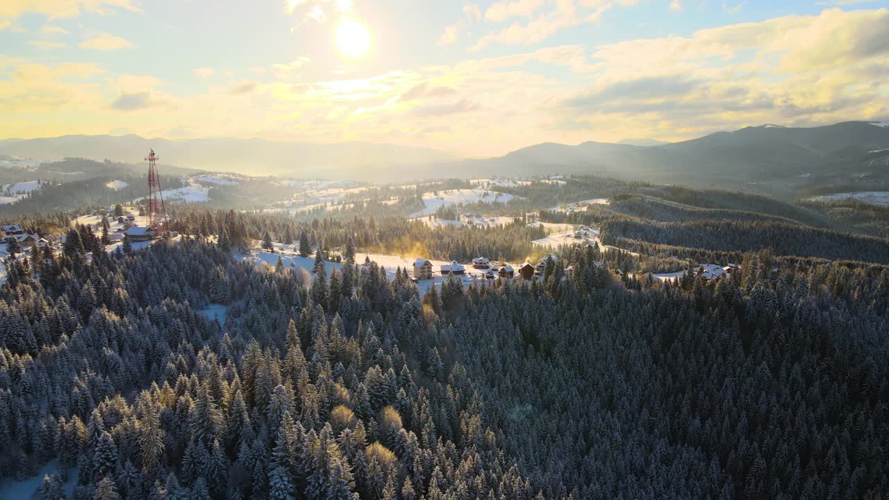 空中冬季景观与小村庄房屋之间的雪覆盖森林在寒冷的山在晚上。视频素材