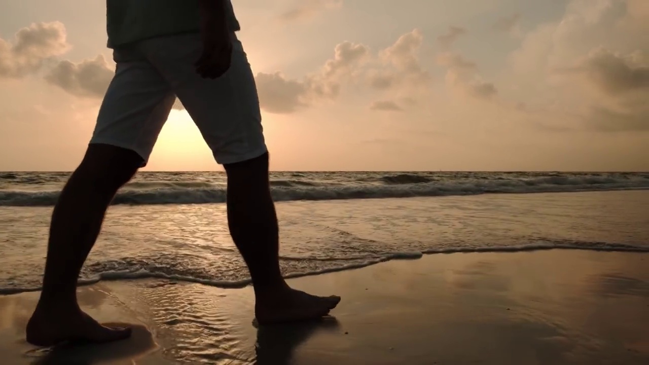 日落时，男性在美丽的海滩上散步的近景。视频素材