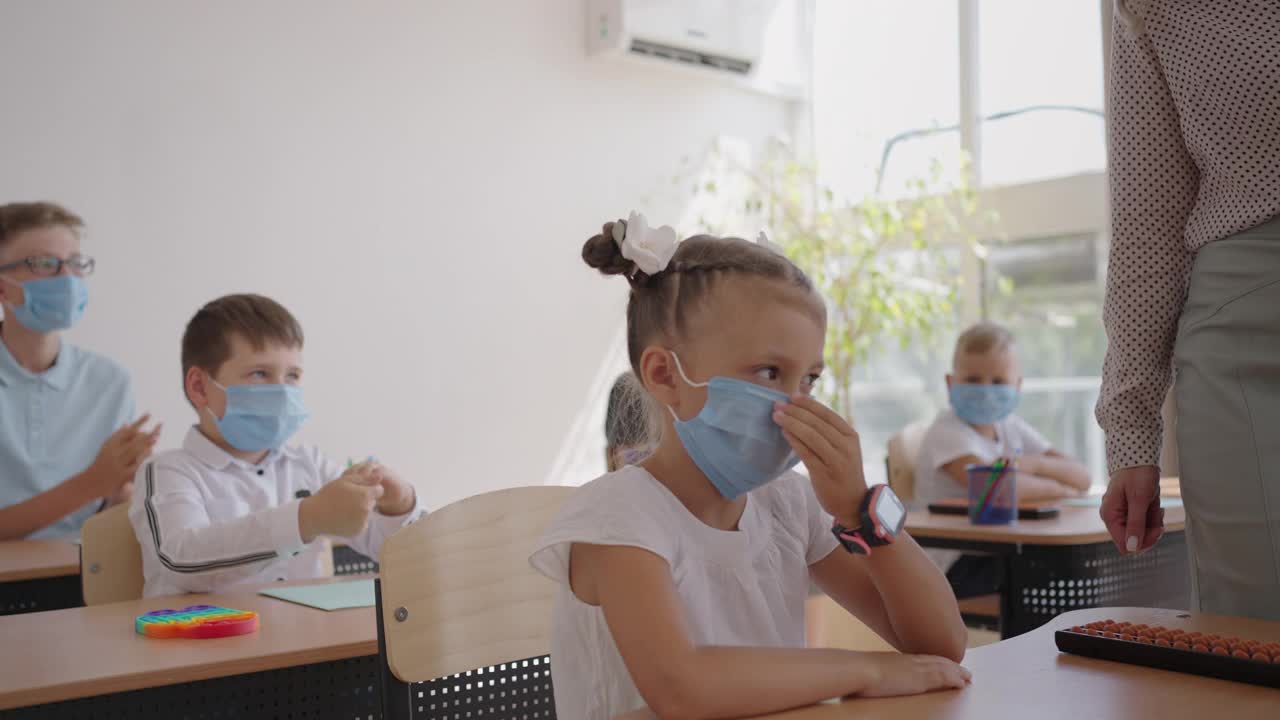 上课前，老师在教室里处理消毒女孩的手。冠状病毒和学校大流行。学校在疫情模式下的工作视频素材