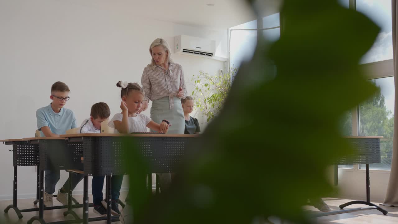 女教师对小学学习过程的控制。一位女教师在课桌之间走动，并负责完成任务视频素材