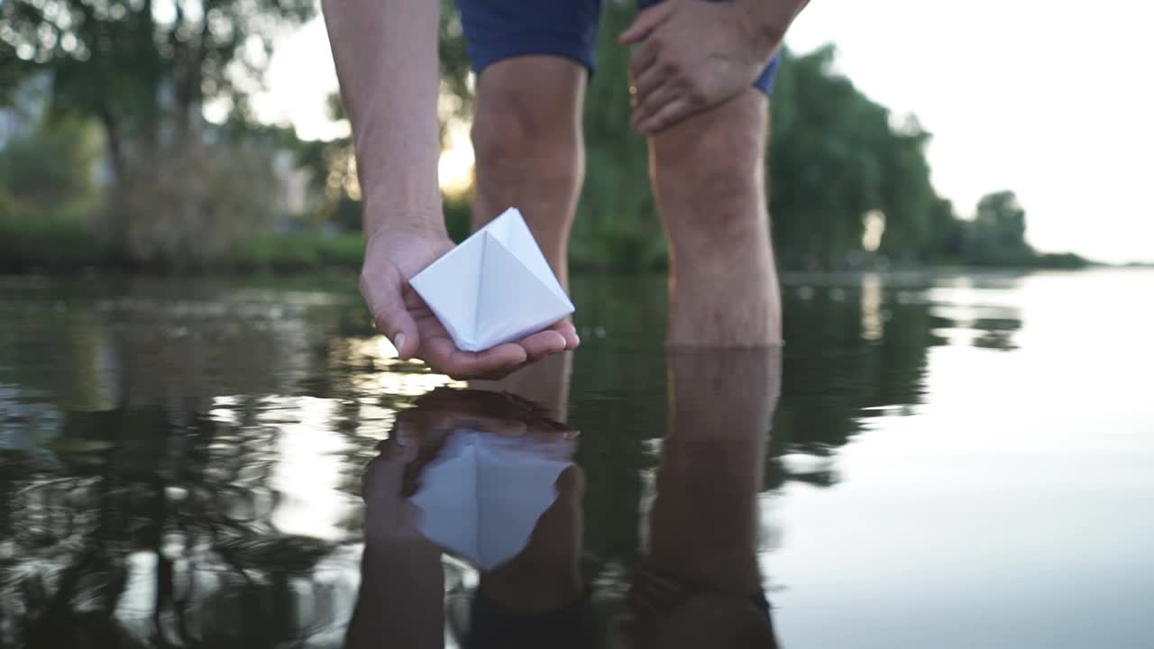 人的手把纸船推到水面上，在美丽的夕阳映照下，将纸船推离大海视频素材