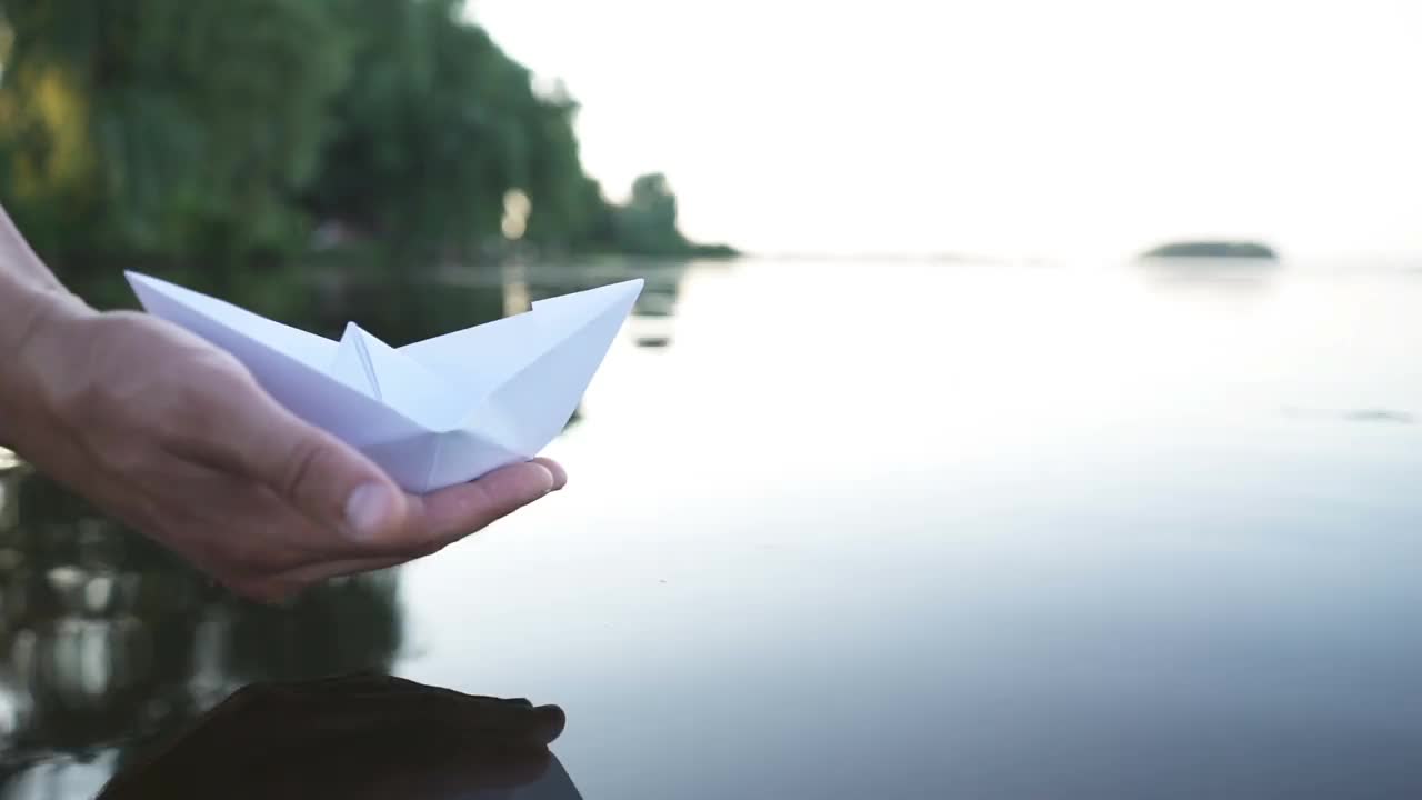 人的手把纸船推到水面上，在美丽的夕阳映照下，将纸船推离大海视频素材