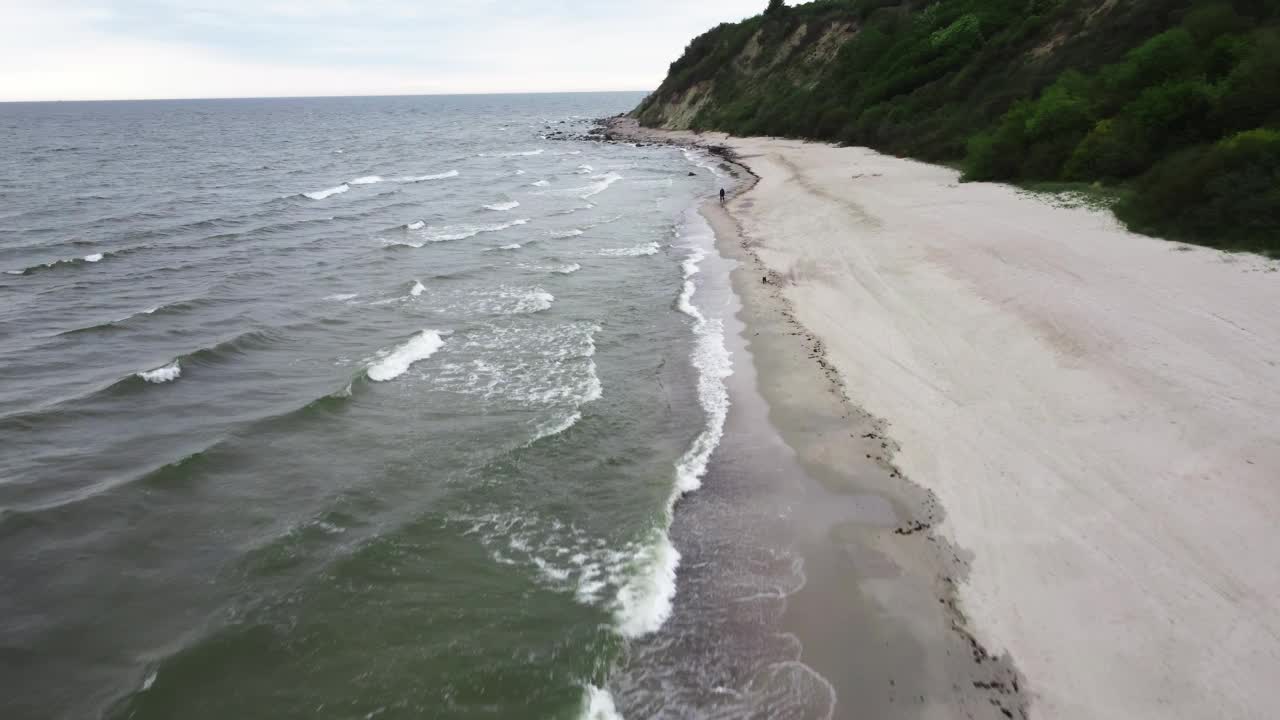 从上面拍摄的画面中，人们在狂暴的海洋和绿色悬崖之间的海岸线上移动视频素材