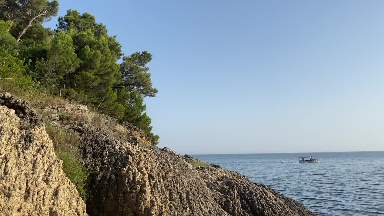 地中海风景优美的岩石海岸。夏天。宁静。黑山。亚得里亚海。美丽的海景。一艘摩托艇在地平线上行驶。悬崖上的松林。视频素材