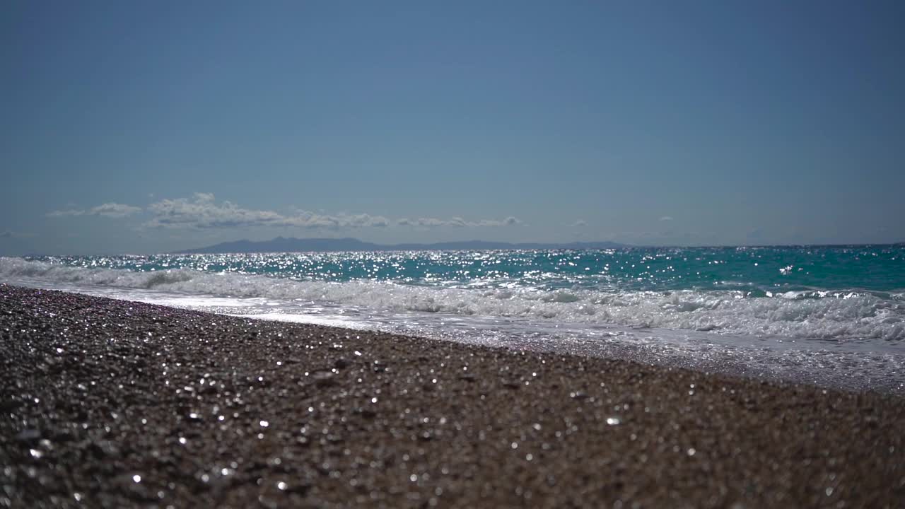 阳光灿烂的日子里，石海岸边的海浪拍打着沙滩，形成白色的泡沫。视频素材