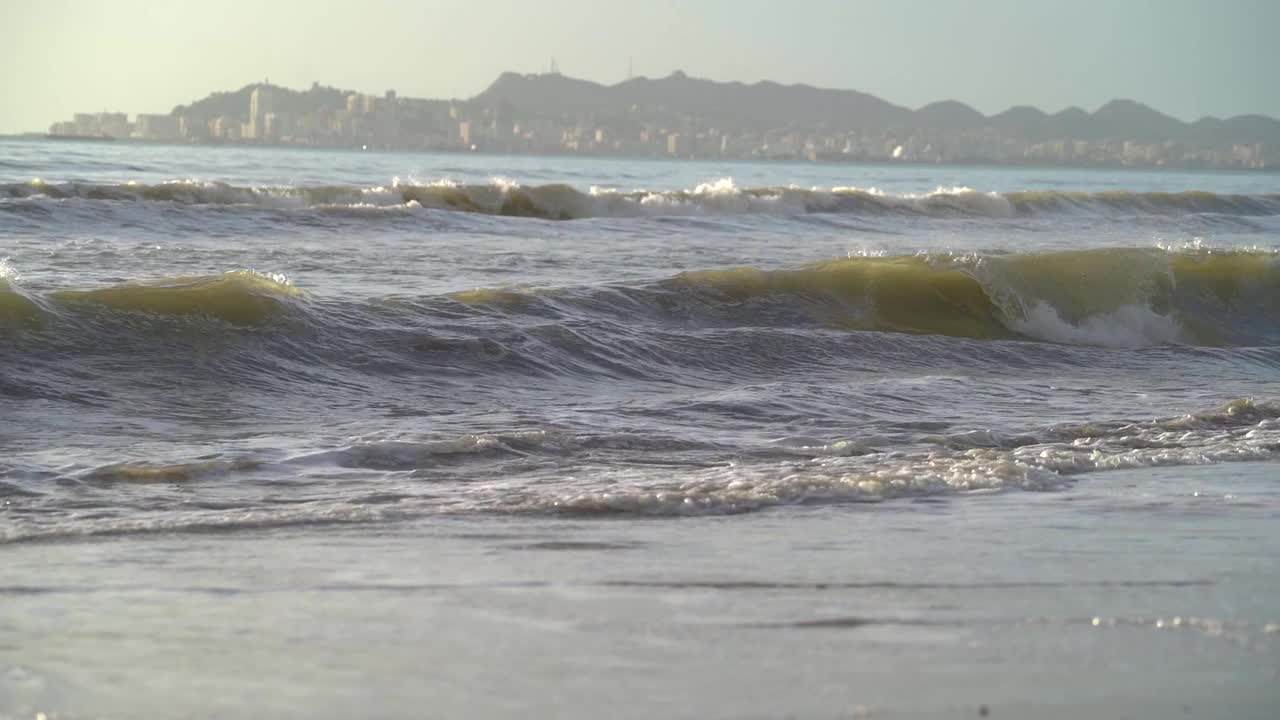 日落海景与长长的海浪和沿海城镇的背景。视频素材