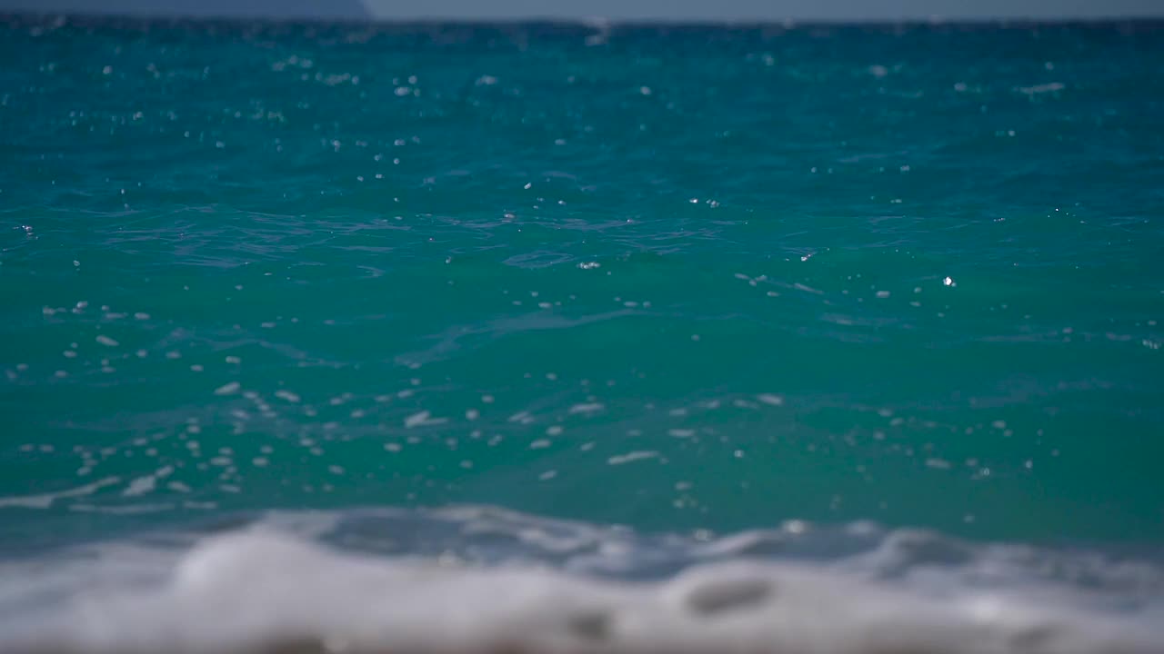 海面上蓝绿色的水与波浪翻滚的管子拍打在海滩上的特写。视频素材