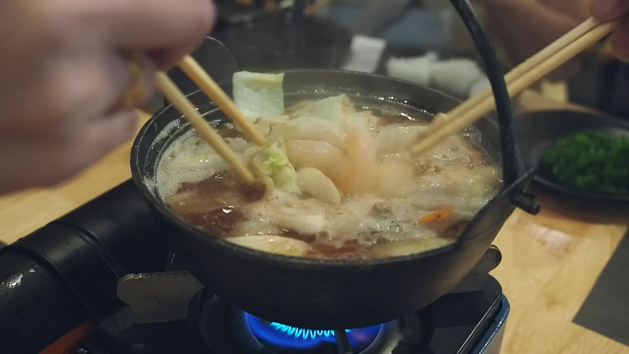 在一家日本餐馆里，餐桌上的每个人都用筷子从涮锅里拿食物。视频素材