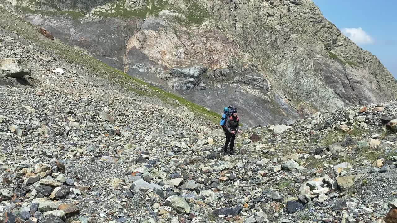 一位年老疲惫的登山游客背着一个大背包沿着山坡走着。视频素材