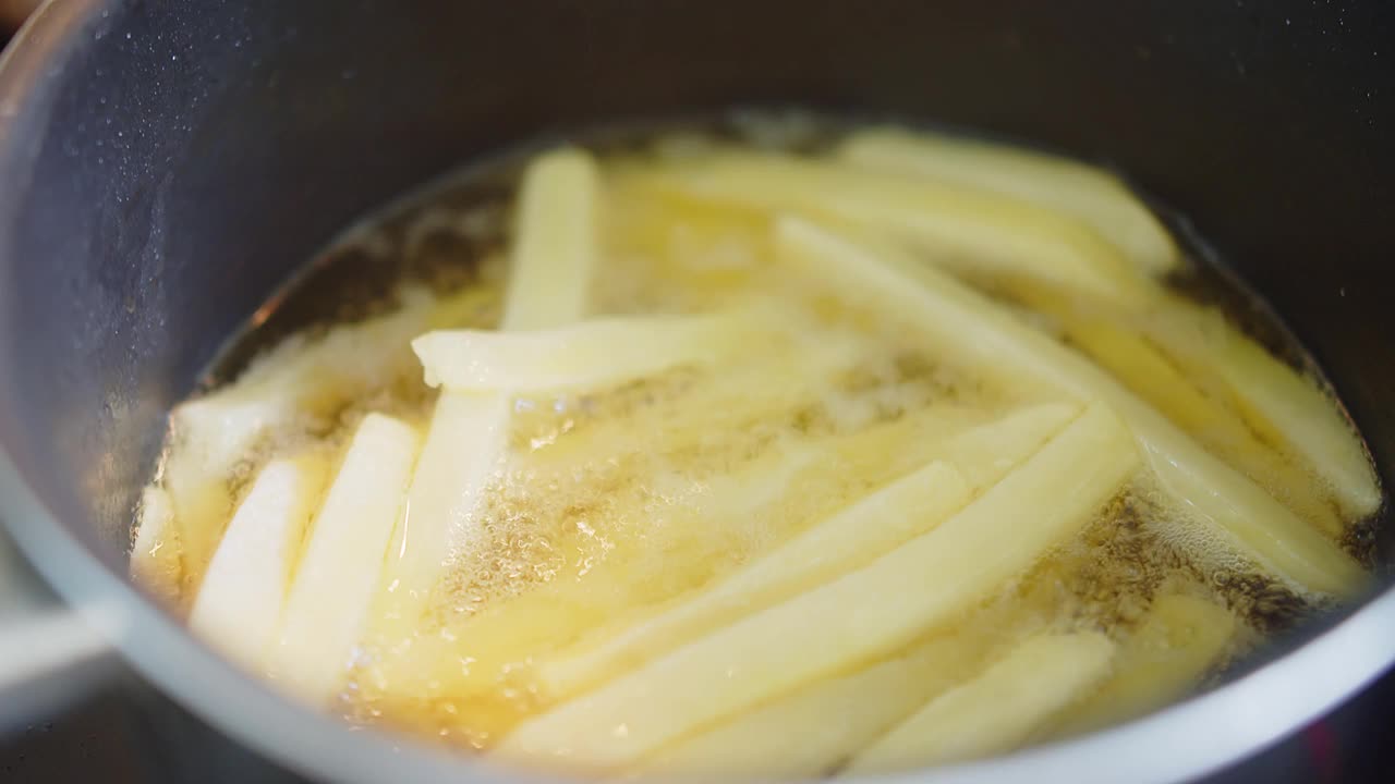 近距离烹饪自制的油炸黄色薯条在厨房的滚烫的泼油土豆，炸出美味的小吃，快餐视频素材