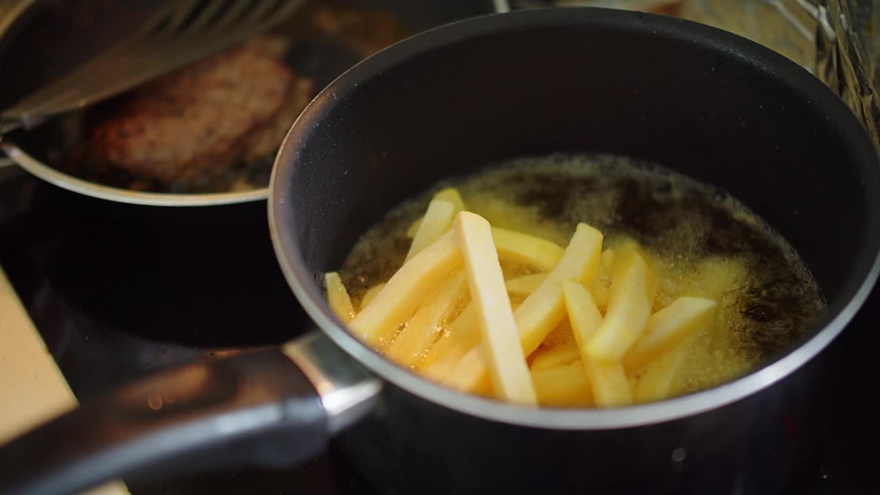 近距离烹饪自制的油炸黄色薯条在厨房的滚烫的泼油土豆，炸出美味的小吃，快餐视频素材