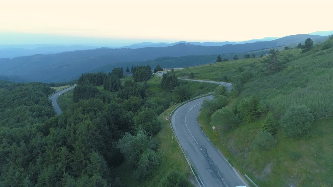 无人机跟踪两辆汽车在弯曲的山路与绿色山谷下面视频素材