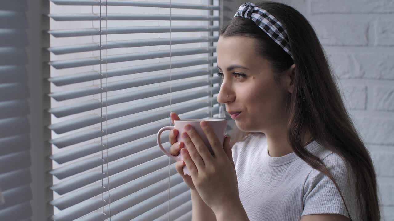 快乐的女人端着茶看着窗外视频素材