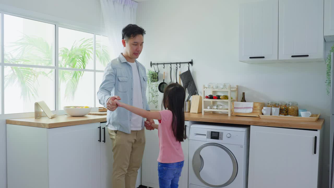 亚洲有魅力的男人父亲喜欢花时间与女儿在家里。爱的父母和小女孩一起跳舞，在家里的厨房里玩耍。保健活动关系概念。视频素材